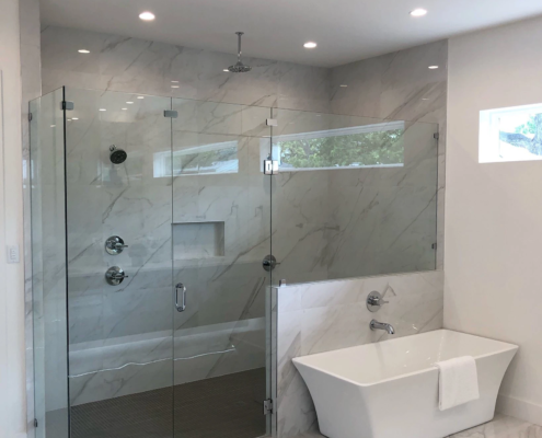 A newly renovated bathroom with marble patterned flooring and walk-in shower; rectangular stand-alone tub