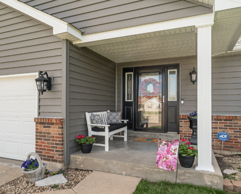The front porch of a home, beautifully adorned with flowers and featuring a cozy bench for relaxation, showcasing the elegant siding replacement.