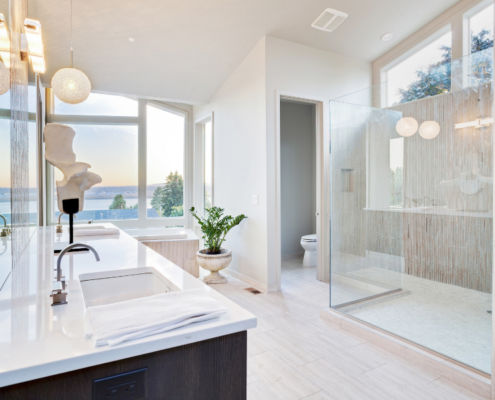 A newly renovated bathroom with very clean, mid-century style. Glass, walk-in shower, dark wood vanity with square dual sinks, large windows that overlook a lake, with a separate water closet.