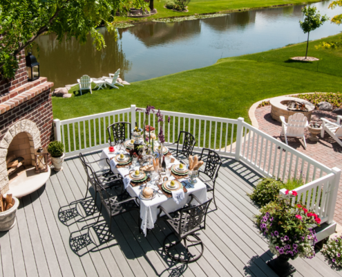 A large deck with a fireplace, a set dining table for 6, overlooking a canal and a green, grassy yard.