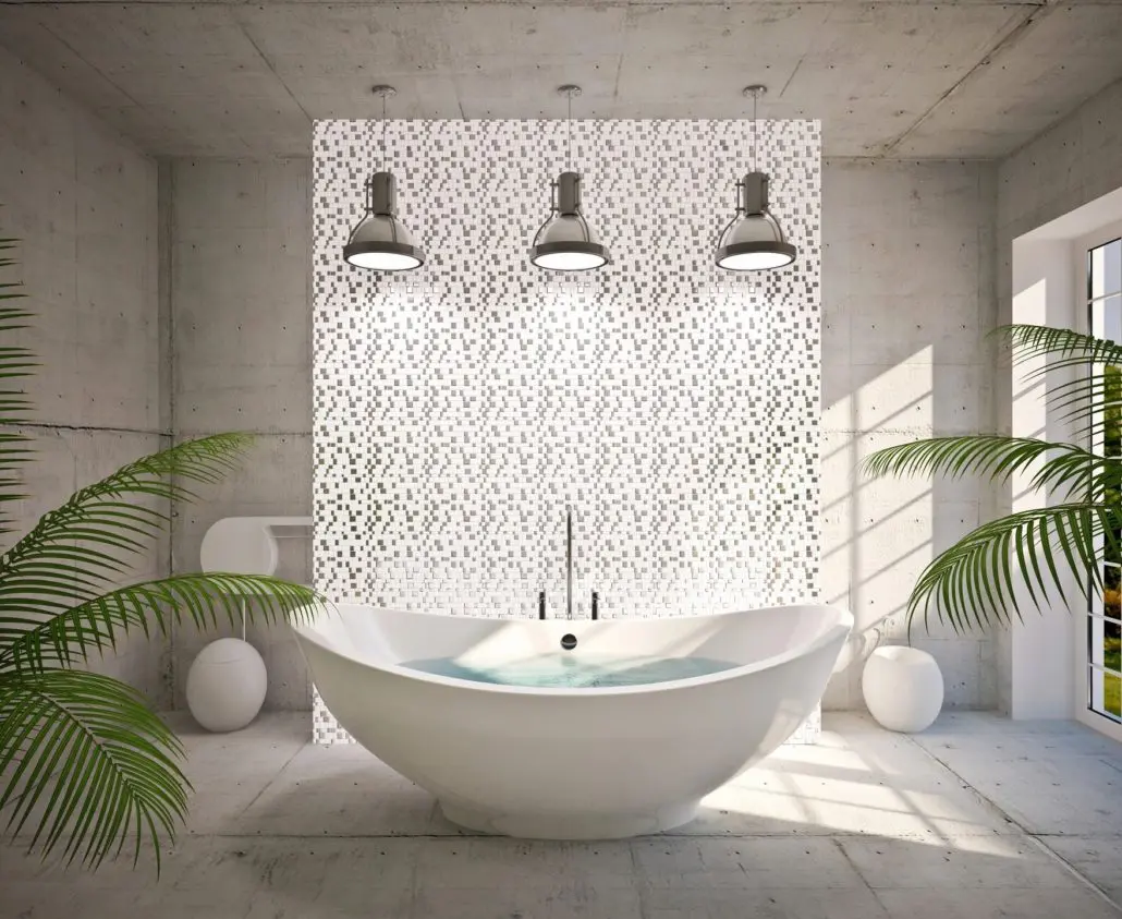 A white stand alone soaker tub with 3 lights overhead on a neutral ceramic tile floor with plants in the frame.