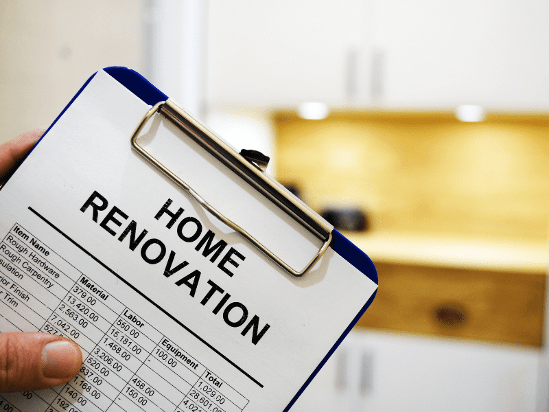 A clipboard being held with a home renovation estimate affixed to it with a kitchen in the background.
