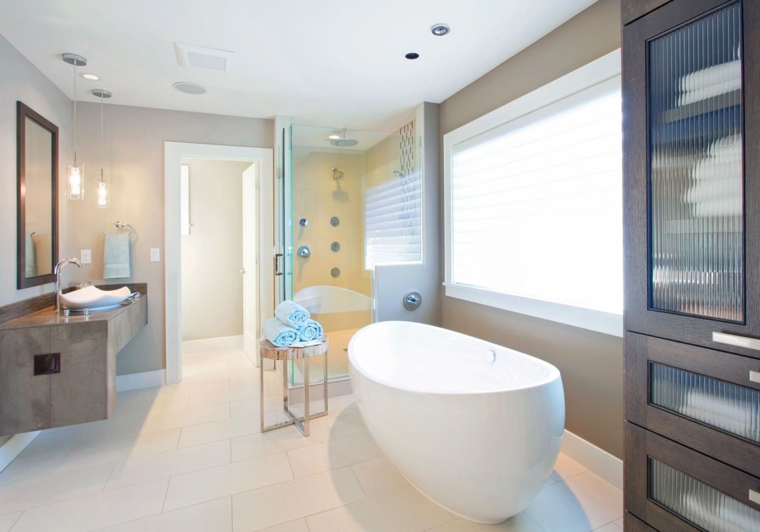 Modern bathroom in white and light tones, with an egg-shaped tsand-alone bathtub, a glass walk-in shower, and a large window. 