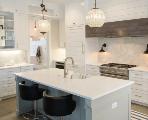 New white Carrera marble kitchen with 2-seater island, pendant lights, and large gas oven.